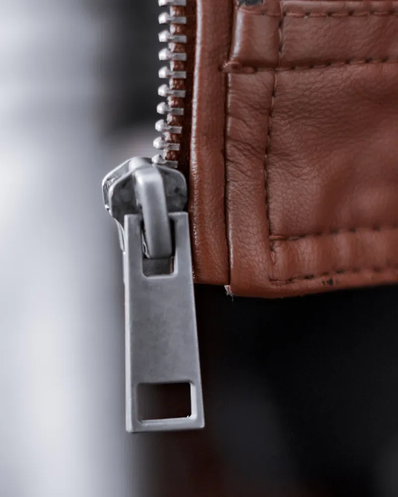 Close-up of a brushed metal zip against the soft grain of a brown leather jacket