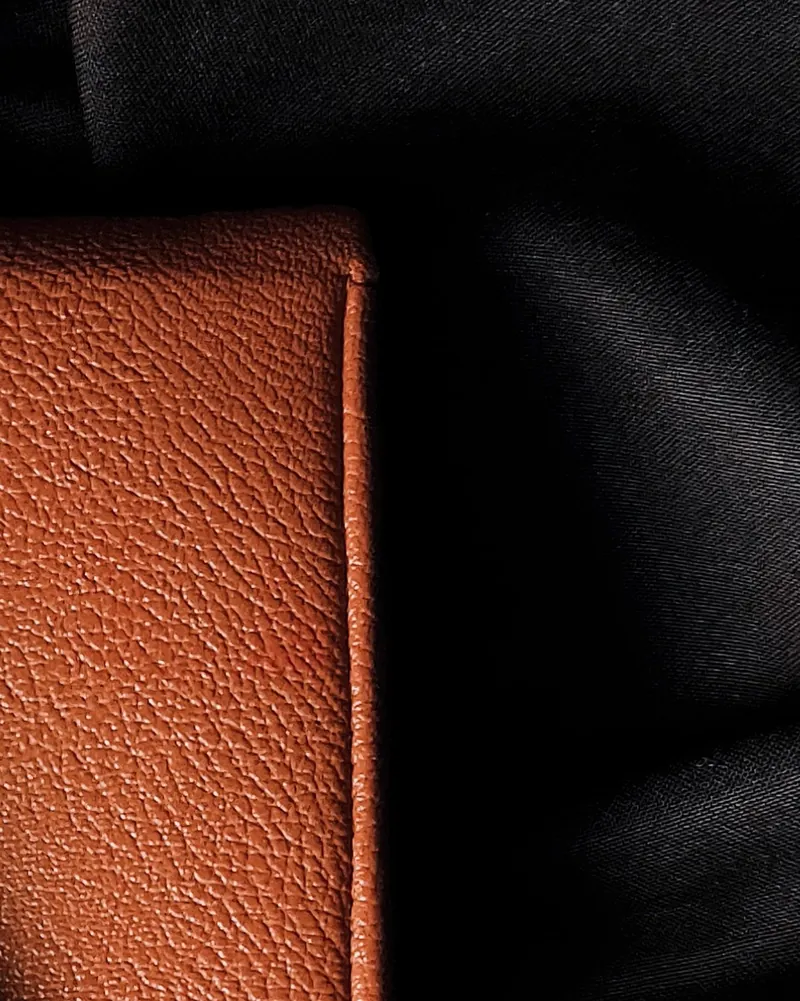 Close-up of a tan pebble-grain card holder, its clean unstitched edge set against black fabric